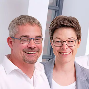 Ein Mann und eine Frau mit Brille und Geschäftskleidung stehen lächelnd in einem Haus. - Bauunternehmen Winsen und Landkreis Harburg