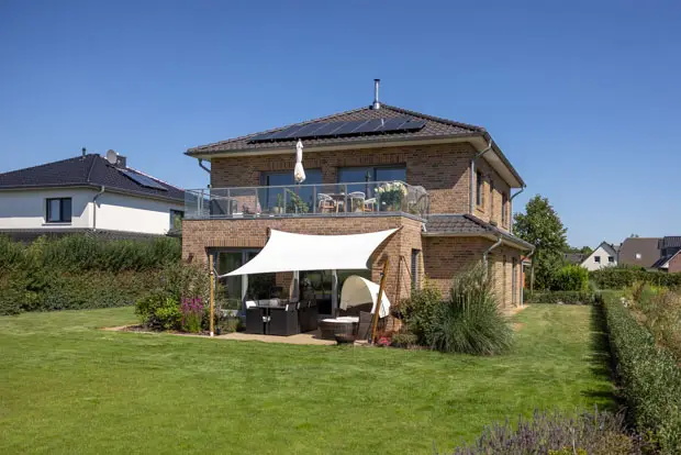 Zweistöckiges Backsteinhaus mit Sonnenkollektoren, großen Fenstern und einer von einem weißen Vordach überdachten Terrasse. - Bauunternehmen Winsen und Landkreis Harburg Zweistöckiges Backsteinhaus mit Sonnenkollektoren, großen Fenstern und einer von einem weißen Vordach überdachten Terrasse. - Bauunternehmen Winsen und Landkreis Harburg